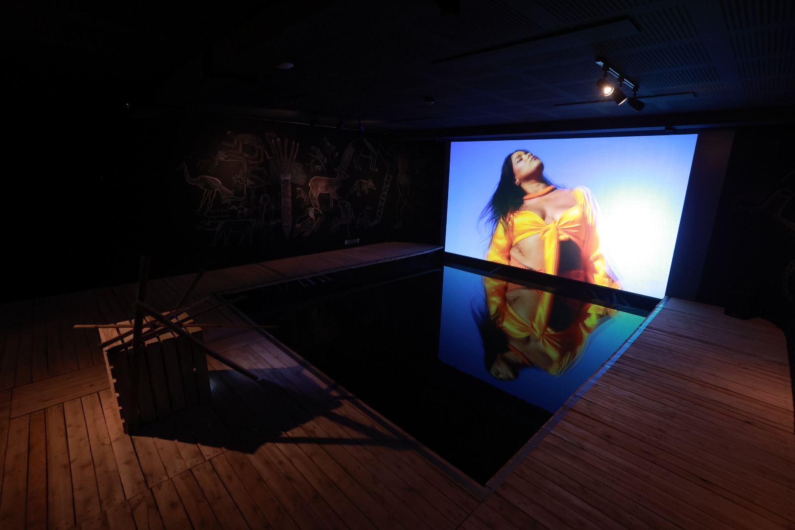 Sala escura com telão mostrando uma mulher indígena